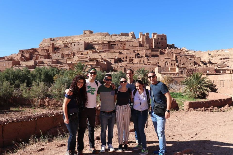 Un grupo de WeRoad posando para una foto frente a un pueblo fortificado histórico construido en la ladera de una colina.
