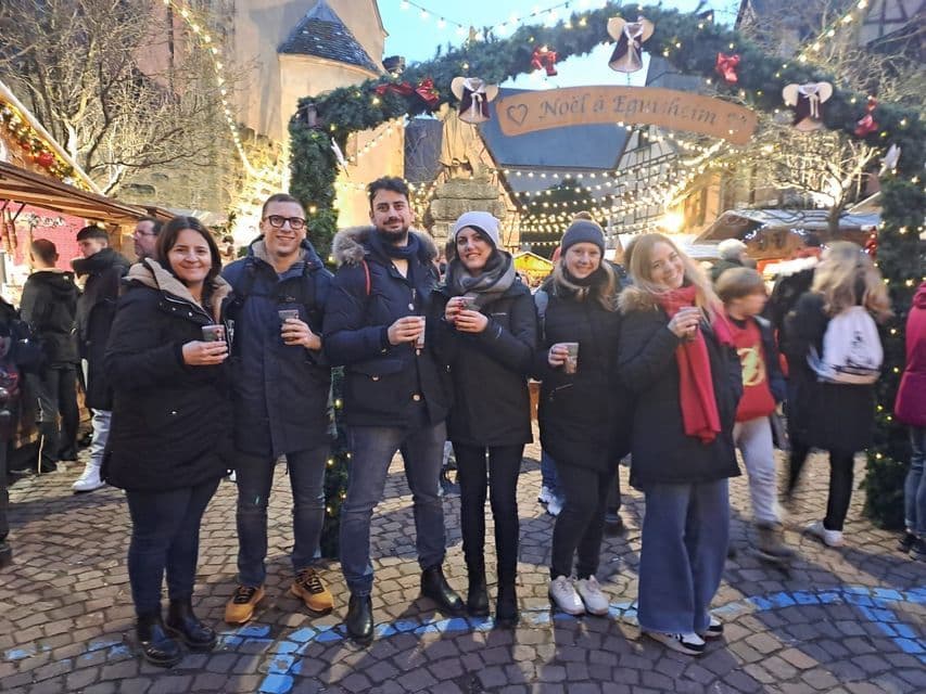 Un viaggio di gruppo WeRoad con bevande in mano e sorridenti sotto le luci festive in un mercato invernale all'aperto
