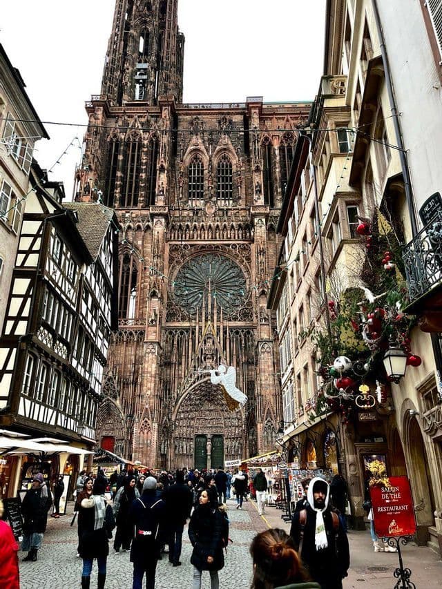 Persone che camminano lungo una strada addobbata fiancheggiata da negozi ed edifici storici verso una imponente cattedrale gotica.