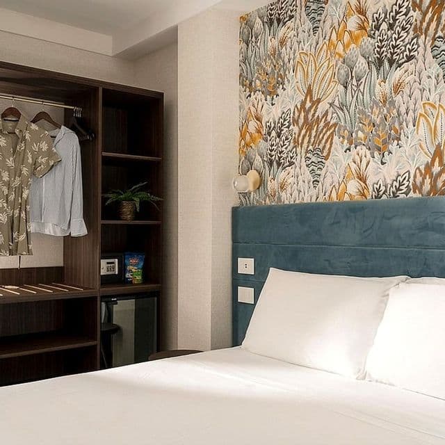 Una camera da letto moderna con un letto dalla testiera blu, carta da parati botanica e un guardaroba in legno aperto.
