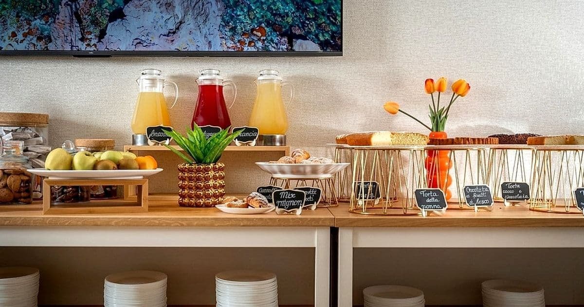 Buffet di colazione con caraffe di succo, frutta fresca, dolci e torte esposti su tavoli di legno.