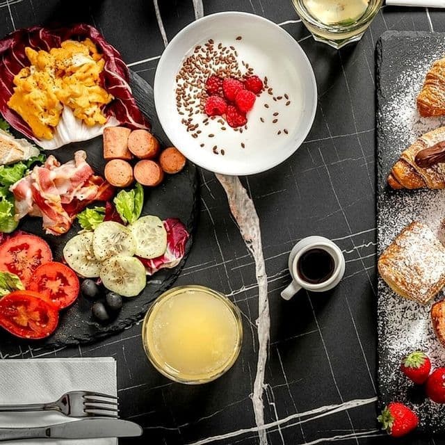 Assortimento per la colazione su un tavolo di marmo nero con uova, salumi, verdure, yogurt con frutti di bosco, dolci e succo di frutta.