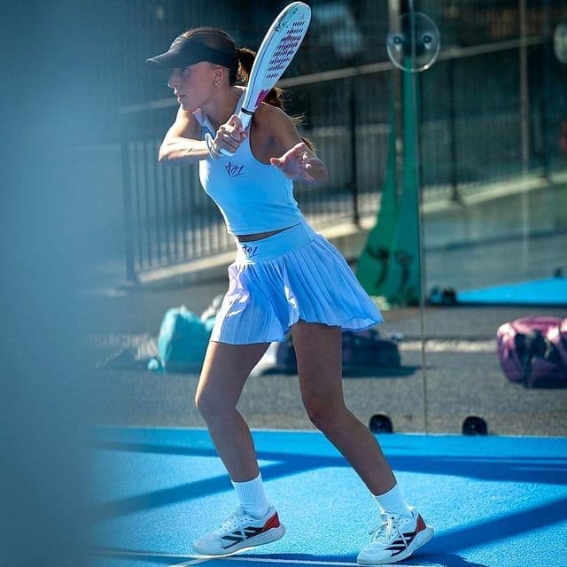 Una donna in abbigliamento sportivo bianco colpisce una racchetta da padel su un campo blu all'aperto