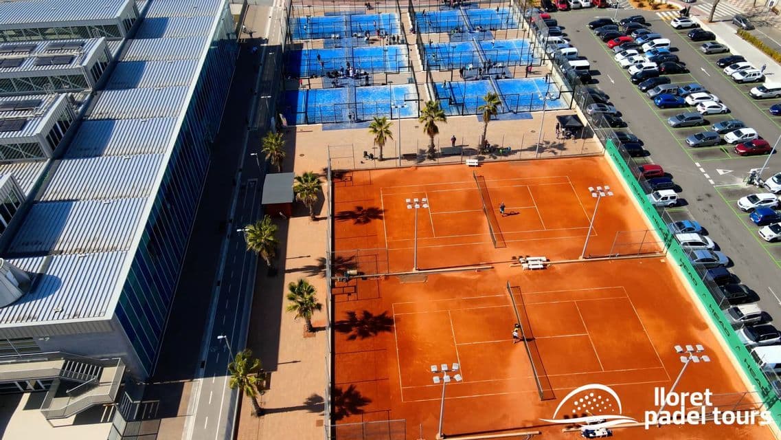 Vista aerea di un complesso sportivo con campi da tennis in terra rossa, campi da padel blu, palme e un parcheggio adiacente