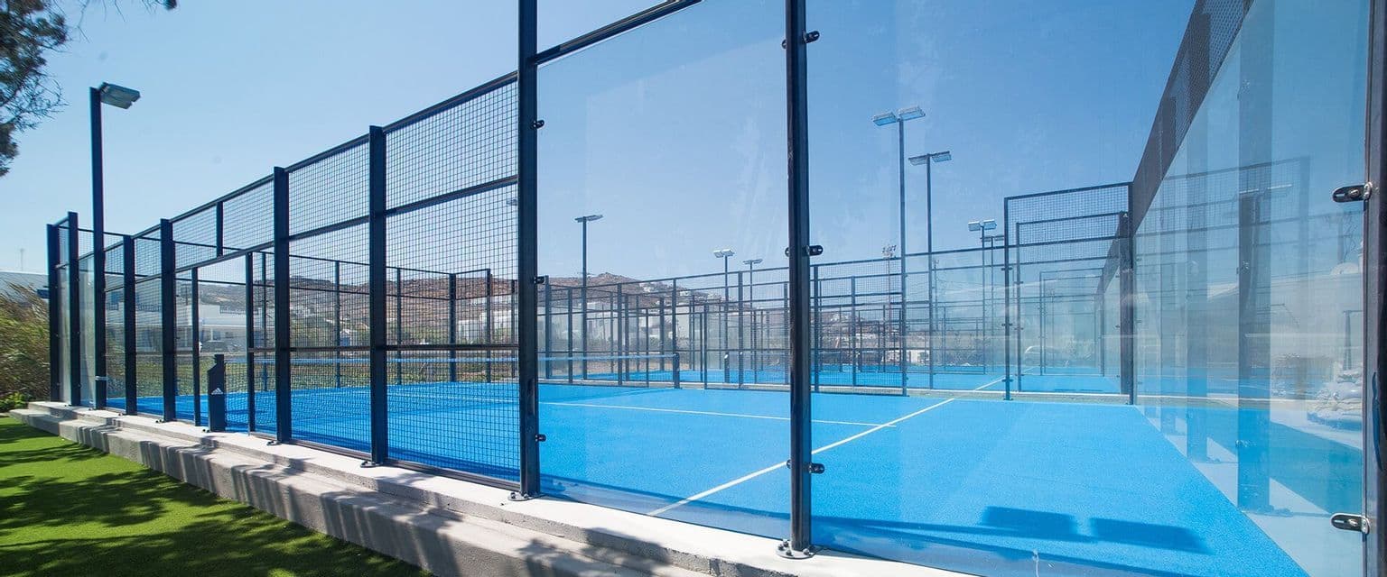 Campi da padel all'aperto vuoti, di colore blu, recintati con pareti di vetro e reti metalliche in una giornata limpida e soleggiata.