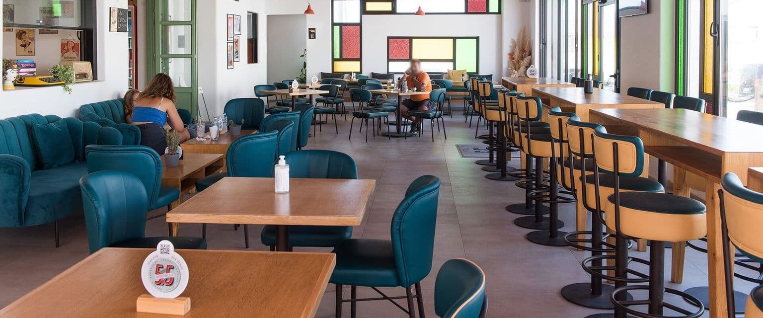 I clienti siedono ai tavoli di legno all'interno di un caffè luminoso e moderno con sedie color tiffany e alti sgabelli da bar.