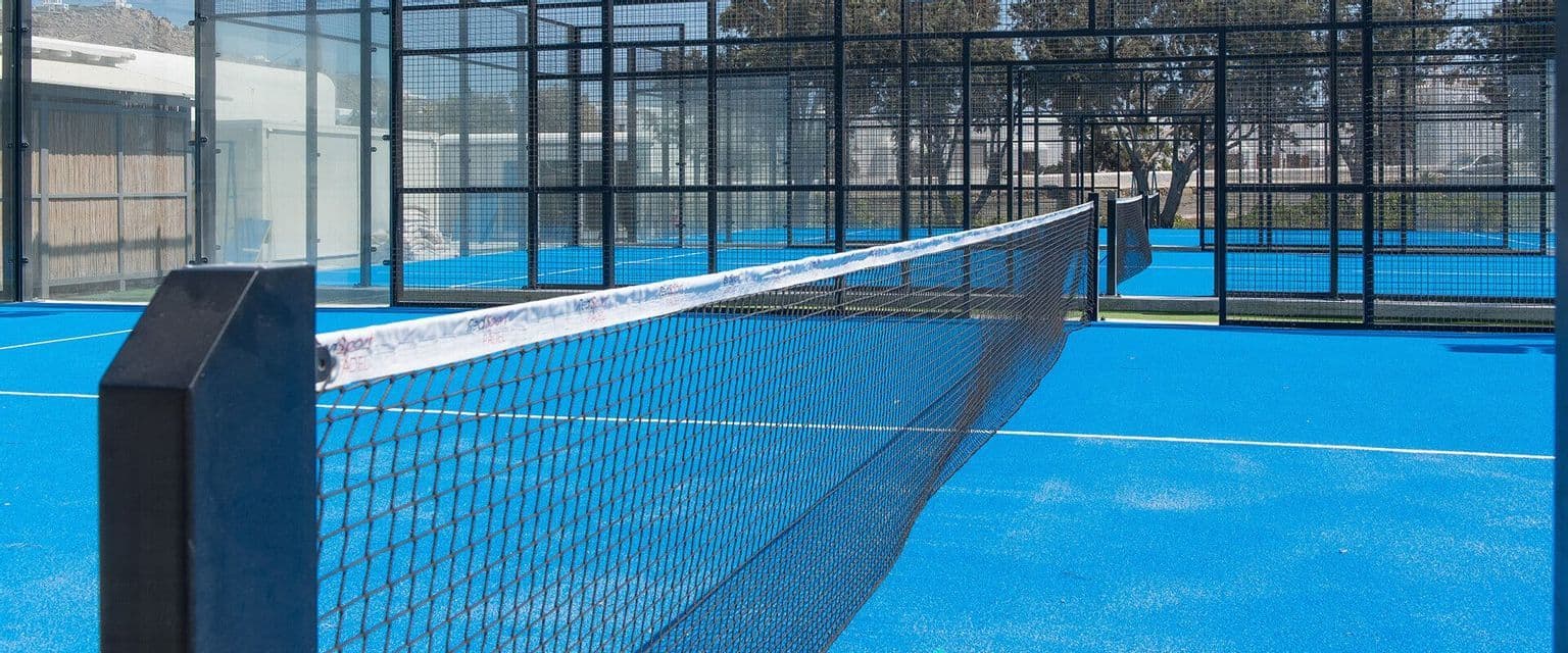 Campo da padel all'aperto vuoto con erba sintetica blu e rete recintata da una rete metallica nera e pareti di vetro