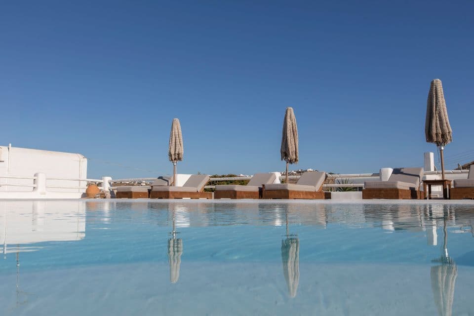 Lettini con ombrelloni chiusi riflessi in una calma piscina sotto un cielo azzurro e limpido