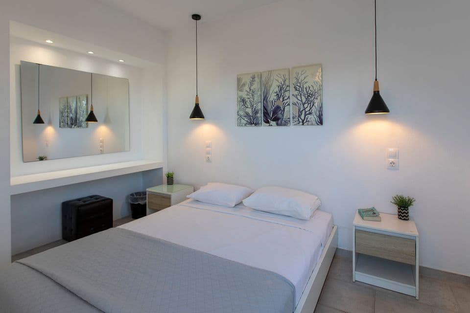 Una camera da letto minimalista bianca con un letto matrimoniale, comodini, lampade a sospensione e un grande specchio da parete