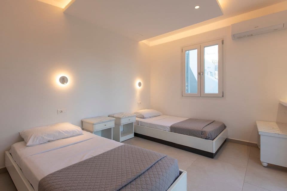 Una camera da letto minimalista con due letti singoli con lenzuola bianche e coperte grigie sotto calde luci a parete