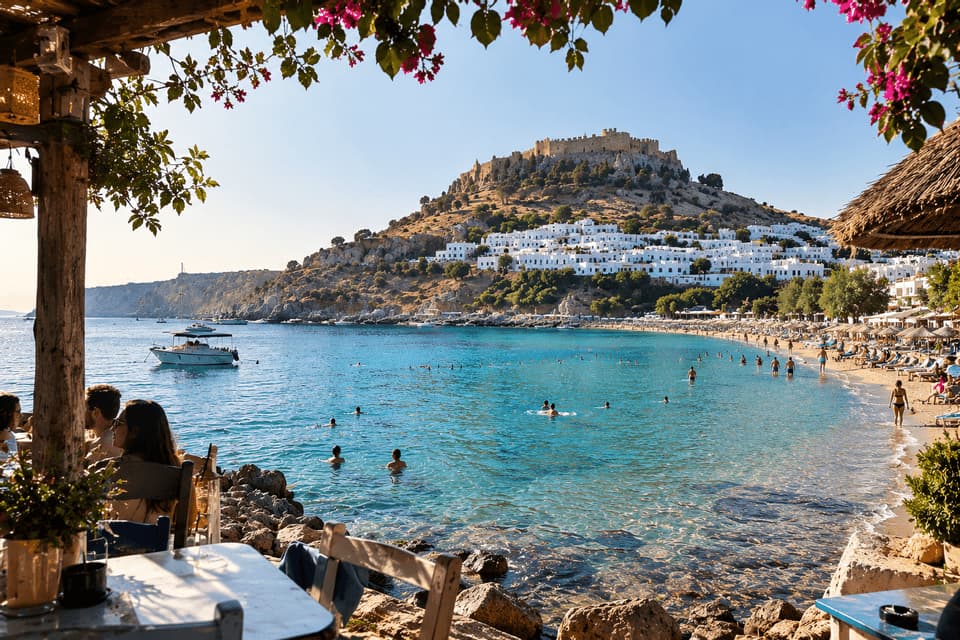 La gente nuota nelle limpide acque costiere vicino a una spiaggia sabbiosa e a una cittadina collinare sormontata da un'antica fortezza.