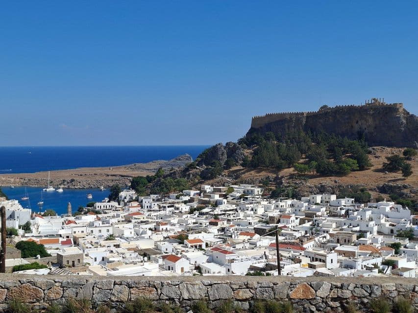 Case imbiancate a calce di un villaggio costiero nascosto sotto un'antica fortezza in cima a una collina accanto a una baia dal mare blu