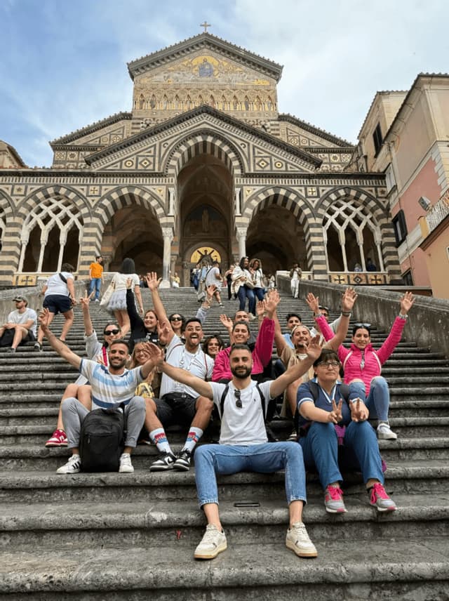Un viaje en grupo de WeRoad sentado en escalones de piedra y saludando frente a una gran catedral