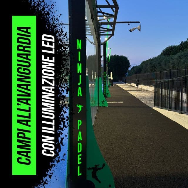 Outdoor padel tennis courts with glass walls and illuminated green posts along a pathway under an evening sky.