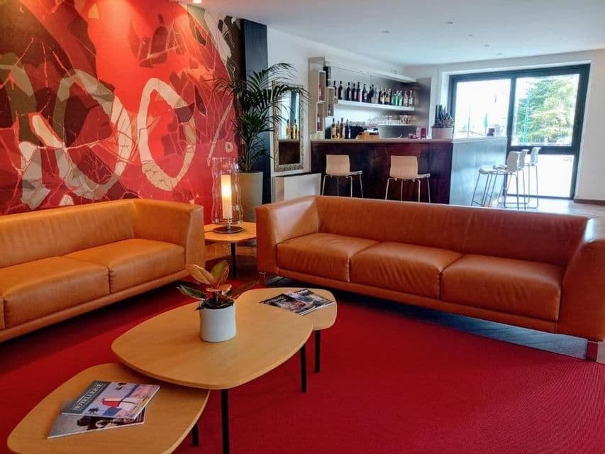 Lounge area featuring brown leather sofas, coffee tables on a red carpet, and a bar counter in the background.