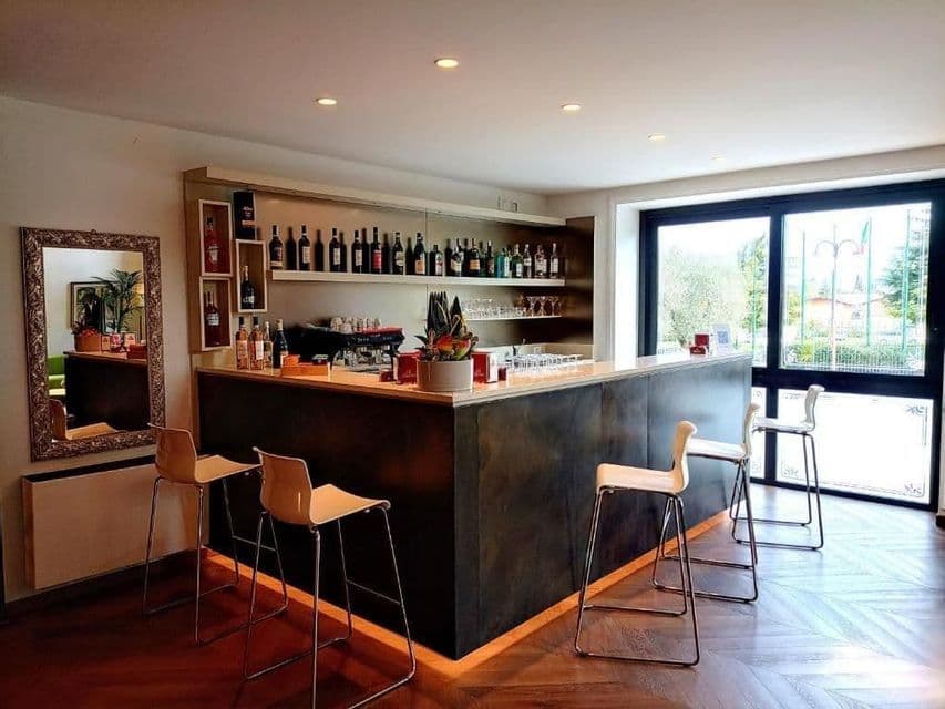 An empty modern bar counter with high white stools, bottle-lined shelves, and wooden flooring indoors.