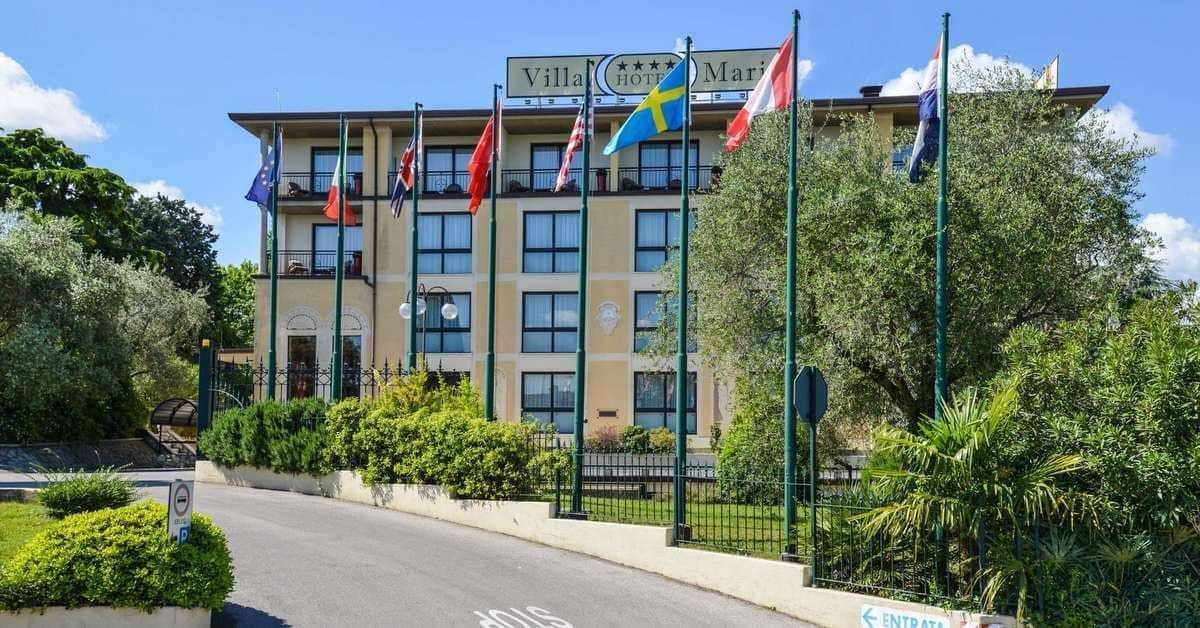 A multi-story hotel building with international flags lining the front driveway surrounded by green trees.