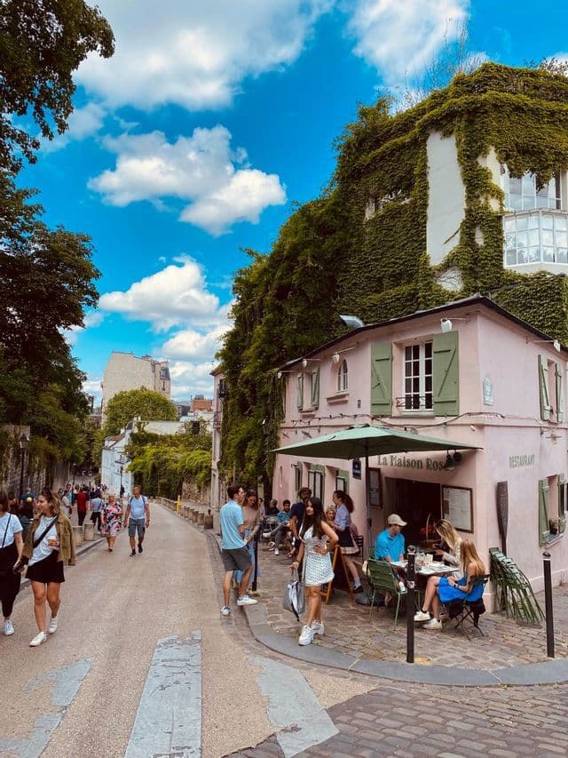 Teilnehmer einer WeRoad-Gruppenreise gehen eine Kopfsteinpflasterstraße entlang, vorbei an einem rosa Restaurant mit Außensitzplätzen.