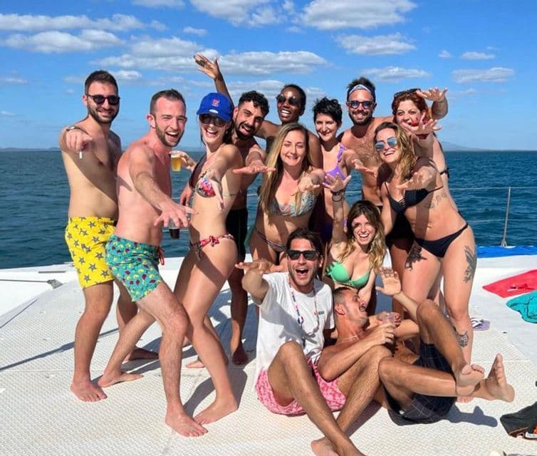 Un numeroso gruppo WeRoad sorride e posa in costume da bagno sul ponte di un catamarano in mare in una giornata di sole.