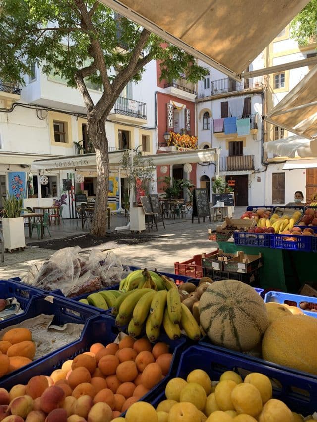 Casse di frutta fresca, incluse albicocche e banane, in una bancarella di mercato all'aperto in una piazza soleggiata.