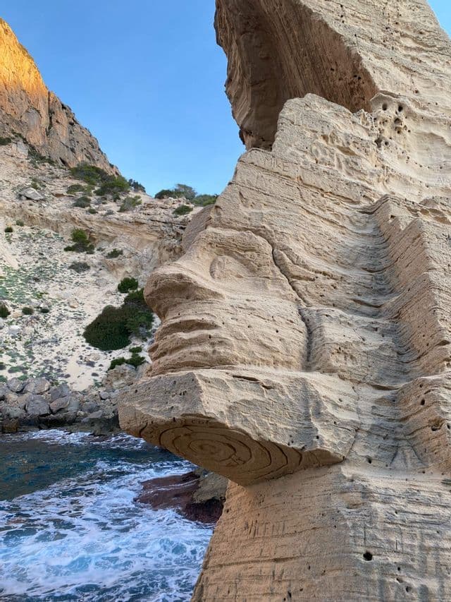 Una scogliera di arenaria consumata, che ricorda un volto umano di profilo, si protende su un mare azzurro e spumeggiante.