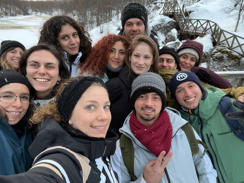Un gruppo WeRoad si fa un selfie sorridente insieme in un paesaggio innevato, vestito con abiti invernali.