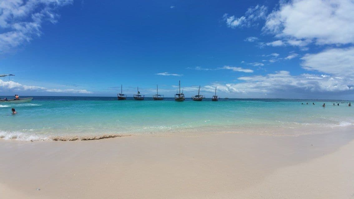 Barche a vela in legno ancorate in acque turchesi limpide al largo di una spiaggia di sabbia bianca sotto un cielo azzurro.