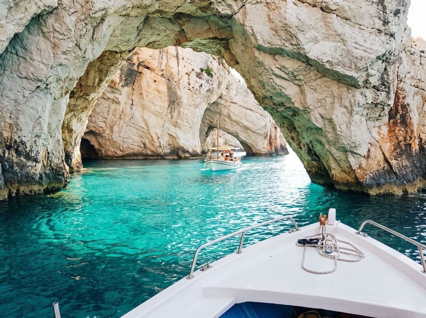 Una vista dalla prua di una barca che naviga in acque turchesi verso grotte marine e archi di roccia calcarea.