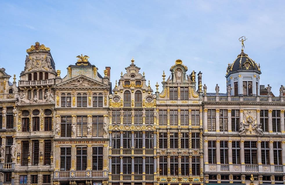 Facciate di edifici storici decorate con ornamenti dorati e statue sotto un cielo azzurro pallido.