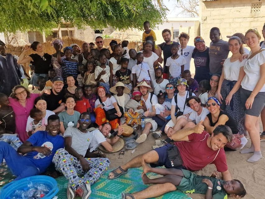 A WeRoad group trip and a local community with many children pose together for a photo in a village.