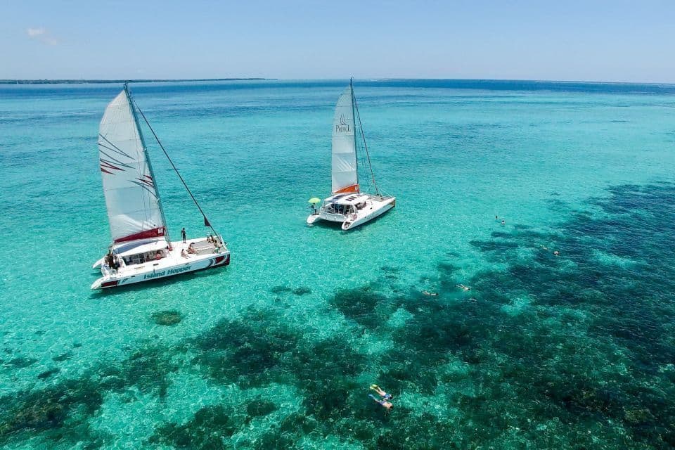 Una vista aerea di un viaggio di gruppo WeRoad su due catamarani, con persone che fanno snorkeling in acque limpide e turchesi su una barriera corallina.