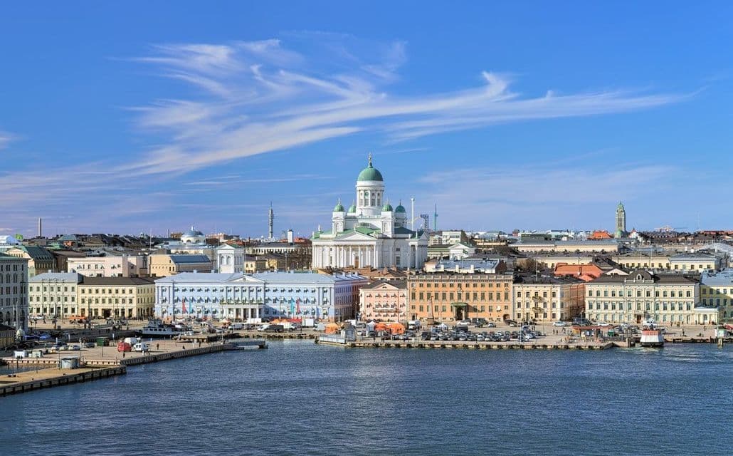Una catedral blanca con una cúpula verde se alza sobre edificios coloridos frente al mar junto a un puerto de la ciudad en un día claro.