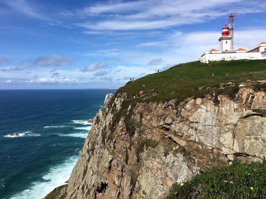 Un groupe WeRoad en randonnée sur une falaise verdoyante face à l'océan, avec un phare blanc et rouge visible sur une colline.