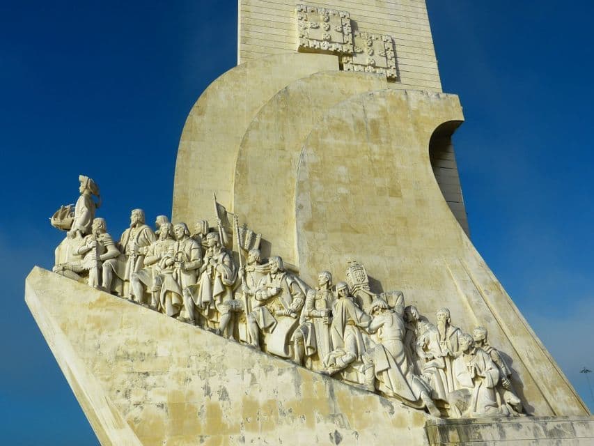 Nahaufnahme historischer Skulpturen auf einem großen Steinmonument vor klarem blauen Himmel, aus der Froschperspektive.