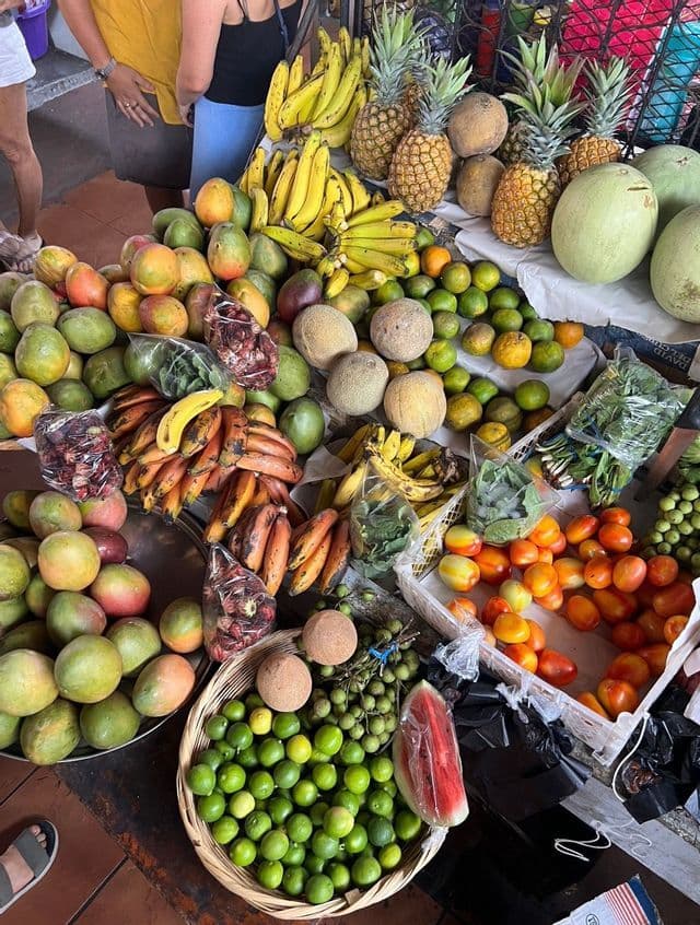 Eine Draufsicht auf einen Marktstand voller frischer tropischer Früchte wie Ananas, Bananen, Mangos und Melonen.