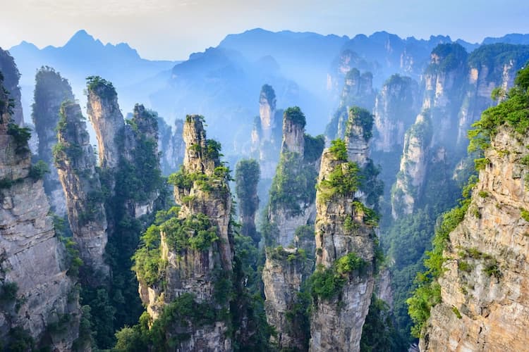 Tall, pillar-like rock formations topped with green foliage, with a hazy mountain range visible in the background.