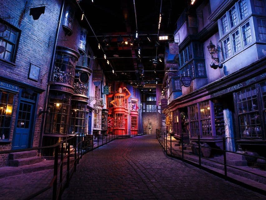 Una strada acciottolata serpeggiante su un set cinematografico, costeggiata da negozi fantastici e storti sotto luci viola e blu suggestive.
