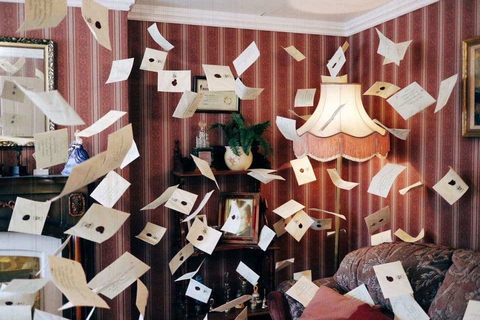 Numerose lettere e buste con sigilli in ceralacca fluttuano nell'aria all'interno di un salotto vintage con carta da parati a righe rosse.