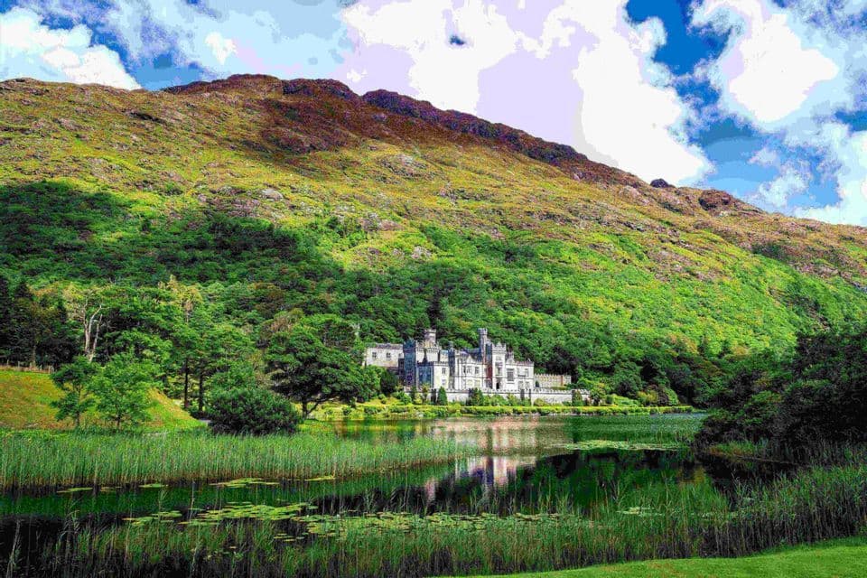 Une abbaye de pierre se dresse sur la rive d'un lac, nichée au pied d'une grande montagne verdoyante et couverte d'arbres.