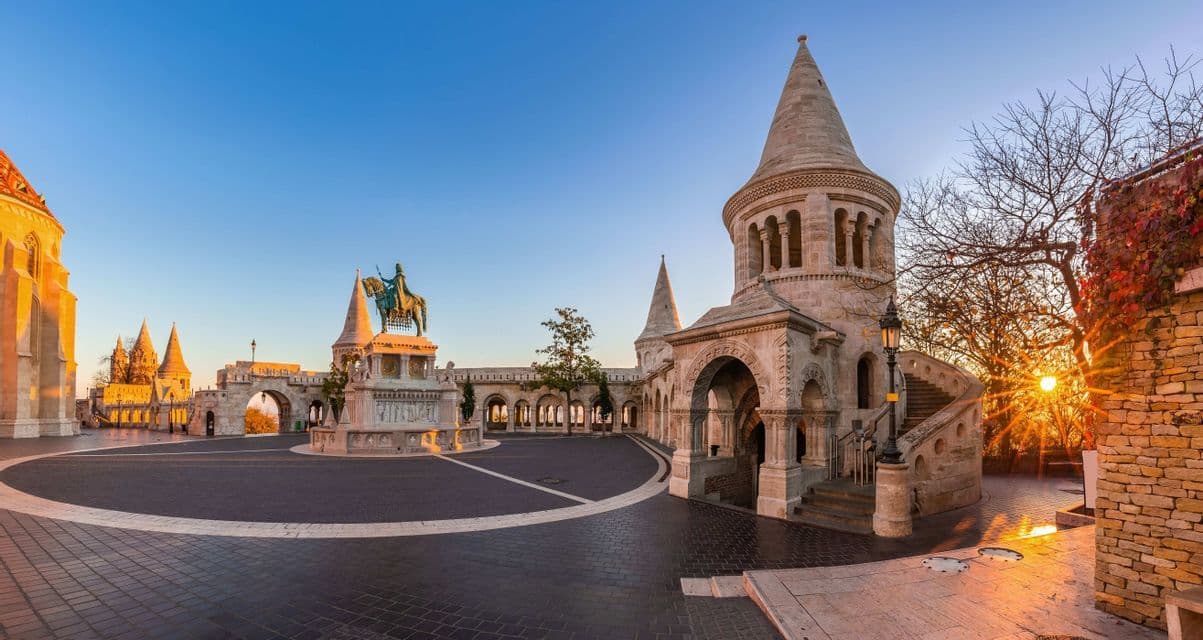Ein Panoramablick auf einen leeren Steinhof mit Türmen und einer Reiterstatue bei Sonnenaufgang.