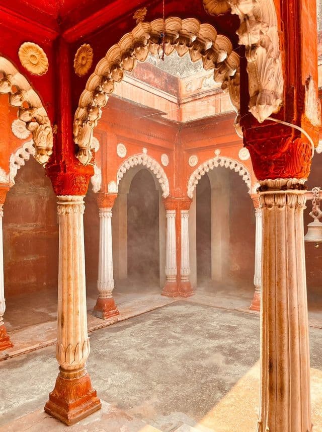 Il cortile interno di un tempio con pareti rosse ornate, pilastri bianchi intagliati e archi a conchiglia, con una leggera foschia nei corridoi.