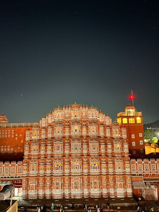 Un palazzo rosa ornato con molte finestre dal design intricato, illuminato di notte sotto un cielo scuro e stellato.