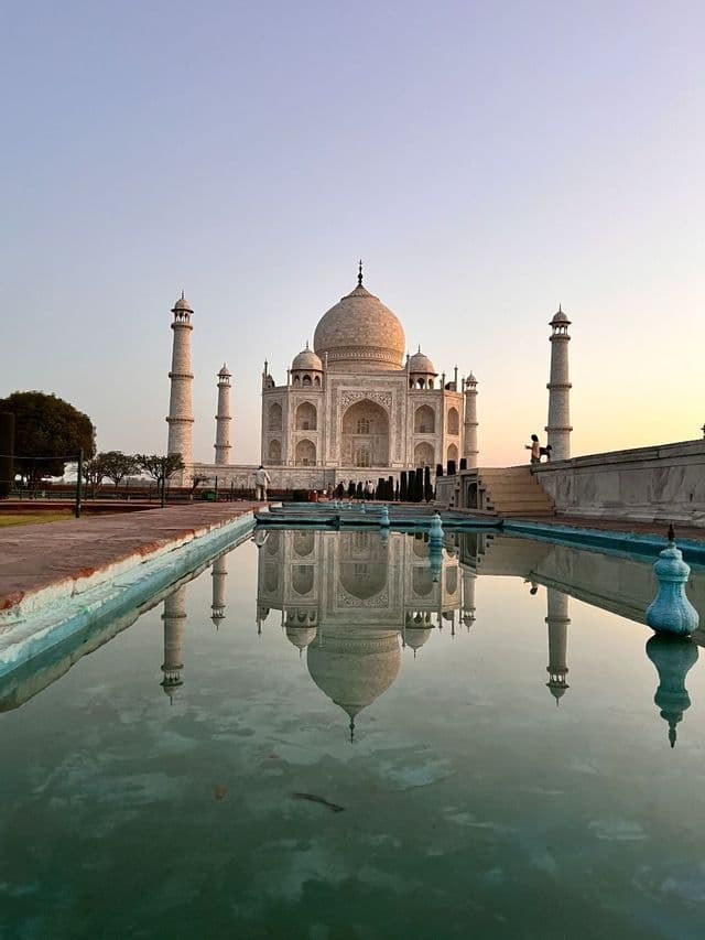All'alba, il Taj Mahal di marmo bianco e i suoi minareti si riflettono perfettamente in una lunga, immobile vasca d'acqua.