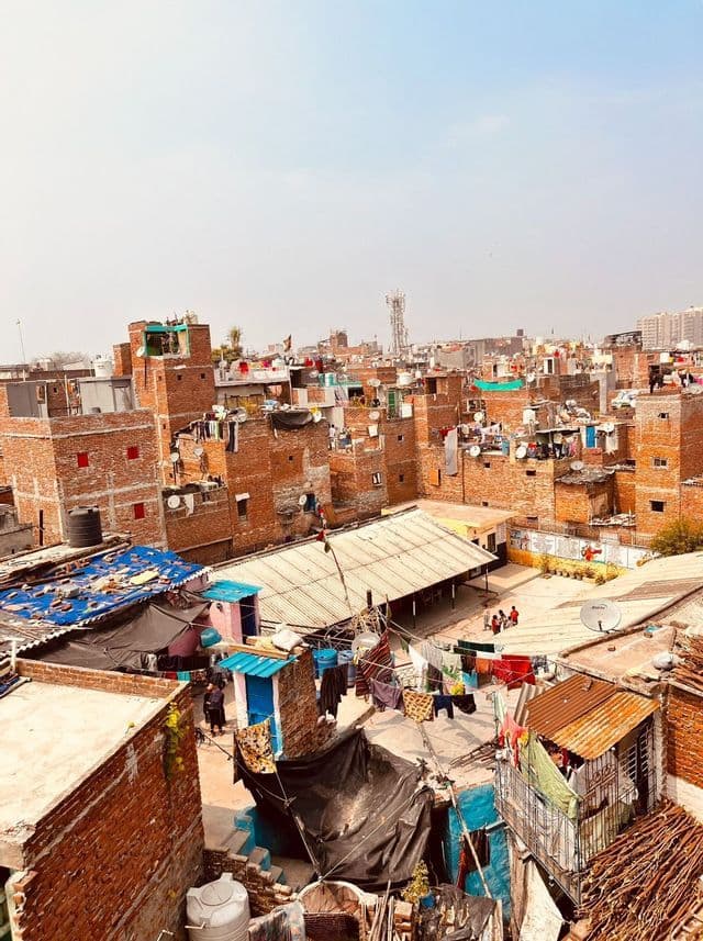 Vista dall'alto di un'area urbana densamente popolata con edifici in mattoni rossi, bucato steso sui tetti e bambini che giocano in un cortile.