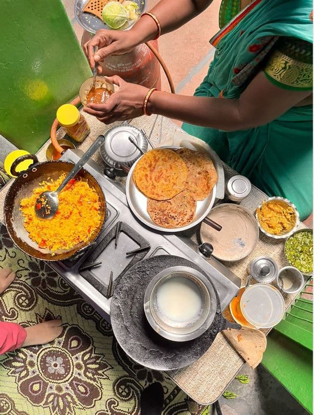 Uno scatto dall'alto di una persona in sari verde che prepara un pasto tradizionale indiano su un fornello a gas con vari piatti.