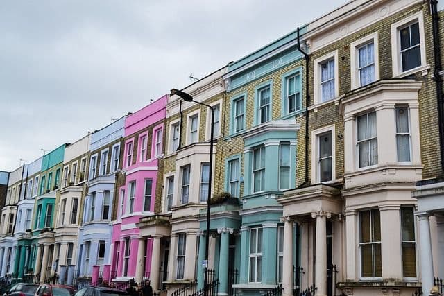 Une rangée de maisons mitoyennes aux façades colorées dans des tons pastel de rose et de bleu sous un ciel nuageux.