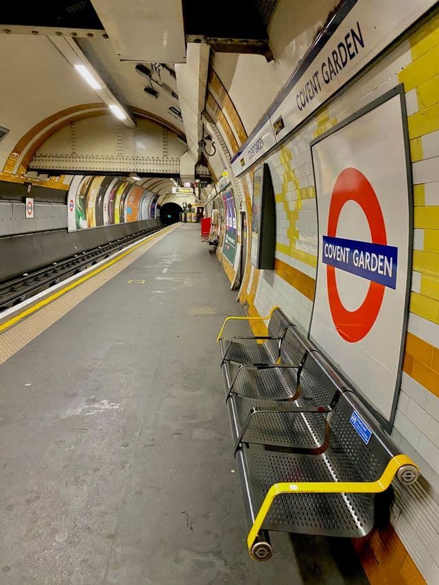 Vue sur un quai vide de la station de métro Covent Garden, avec des bancs en métal et le panneau rond emblématique.