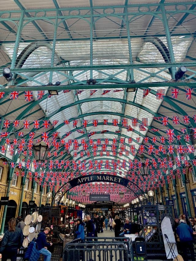 Des acheteurs déambulent dans le marché aux pommes sous un toit de verre cintré décoré de nombreuses guirlandes de drapeaux britanniques.