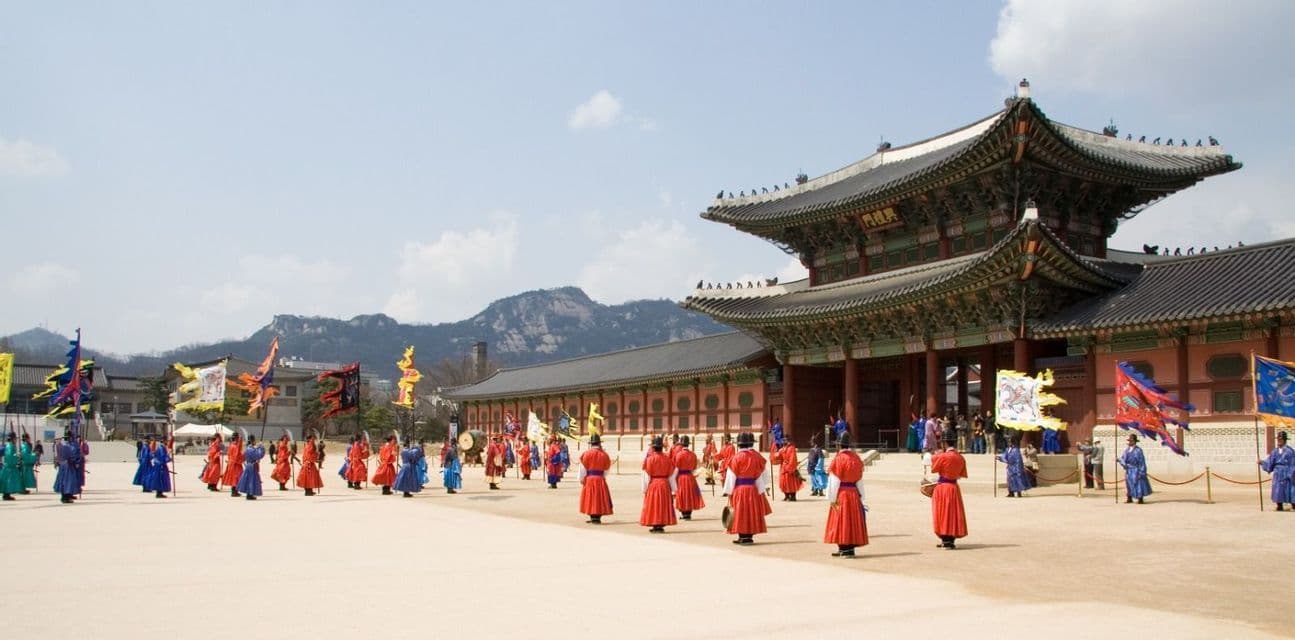 Guardias con vistosos trajes tradicionales se mantienen en formación durante una ceremonia en el patio de un palacio, con montañas de fondo.