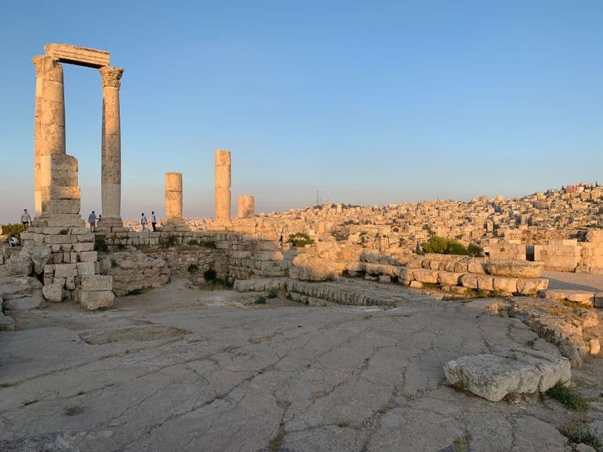Un groupe WeRoad se tient parmi d'anciennes ruines de pierre aux hautes colonnes, surplombant une ville étendue sur une colline au coucher du soleil.